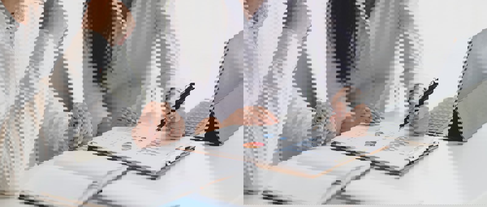 A woman showing her colleague, both wearing plain white shirts, some charts on a clipboard.