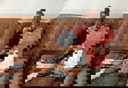 A child leaning against his father, both using mobile phones. They are sitting on a brown leather sofa.