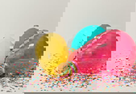 Yellow, teal and pink balloons against a confetti background.