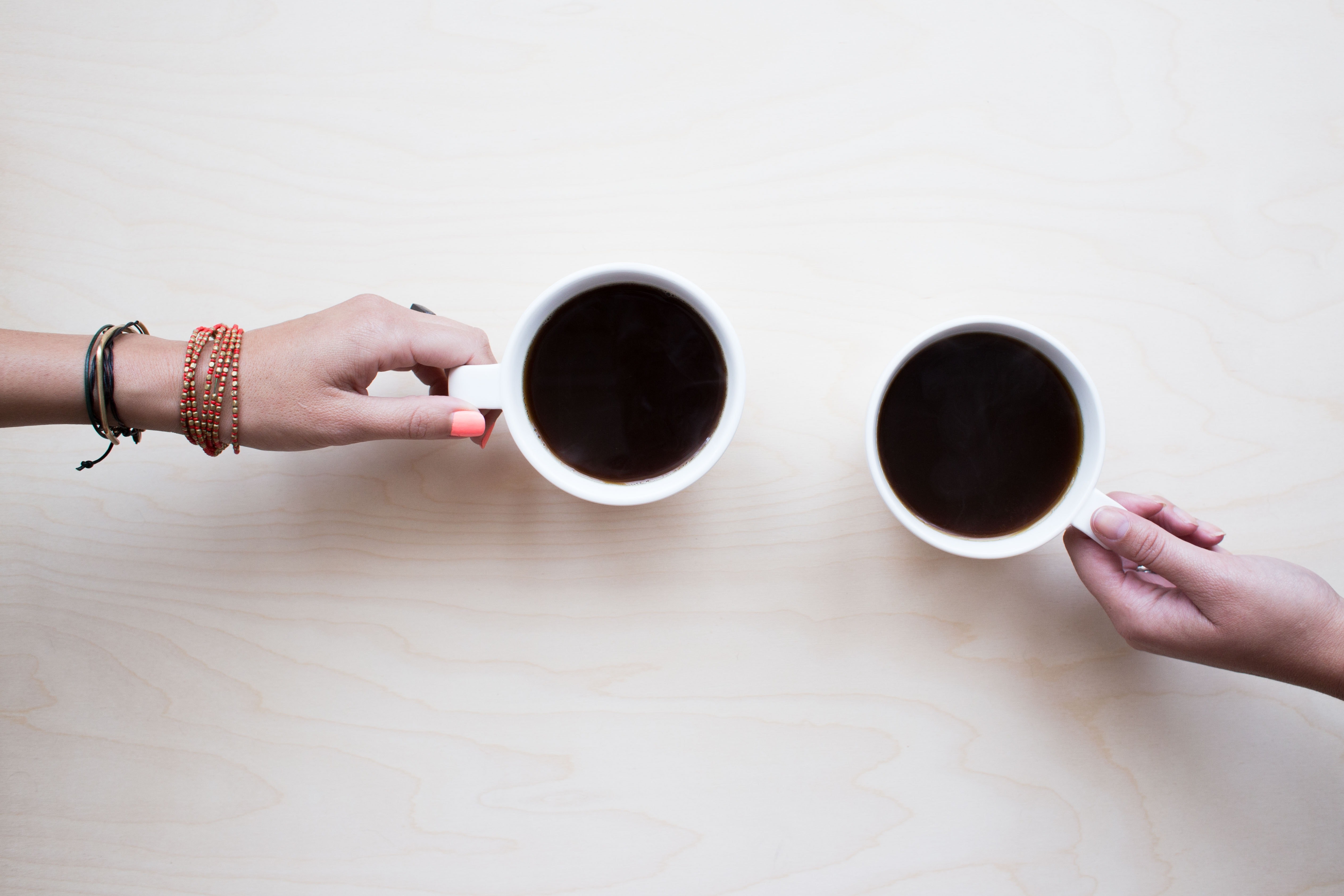 A shot from above of two mugs of black coffee, with a hand resting on each mug