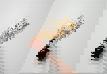 Photograph of a black piggy bank surrounded by cons with someone's hand dropping a coin in