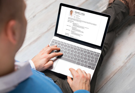 Photograph looking over the shoulder of a man working on his CV on a laptop