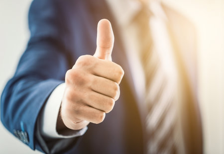 Close up of a man in a suit making a thumbs-up gesture towards the camera