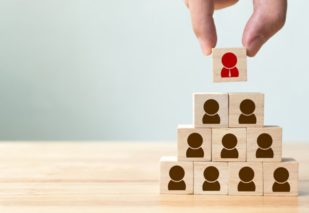 Photograph of ten wooden blocks with an icon on a person printed on the front face, stacked in a pyramid. The top one is a different colour and just being added to the stack.