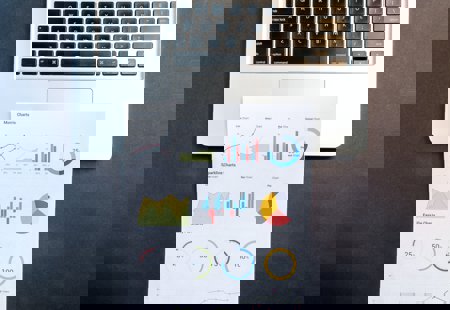 Photograph of a laptop with a printout of various charts lying across the trackpad