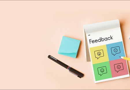 Photograph taken from overhead of someone holding a pencil to write on a notepad which is headed 'Feedback'