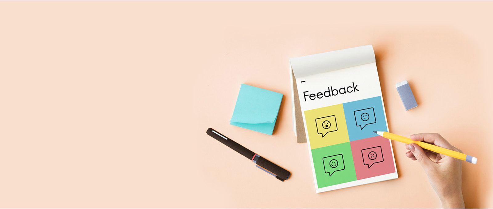 Photograph taken from overhead of someone holding a pencil to write on a notepad which is headed 'Feedback'