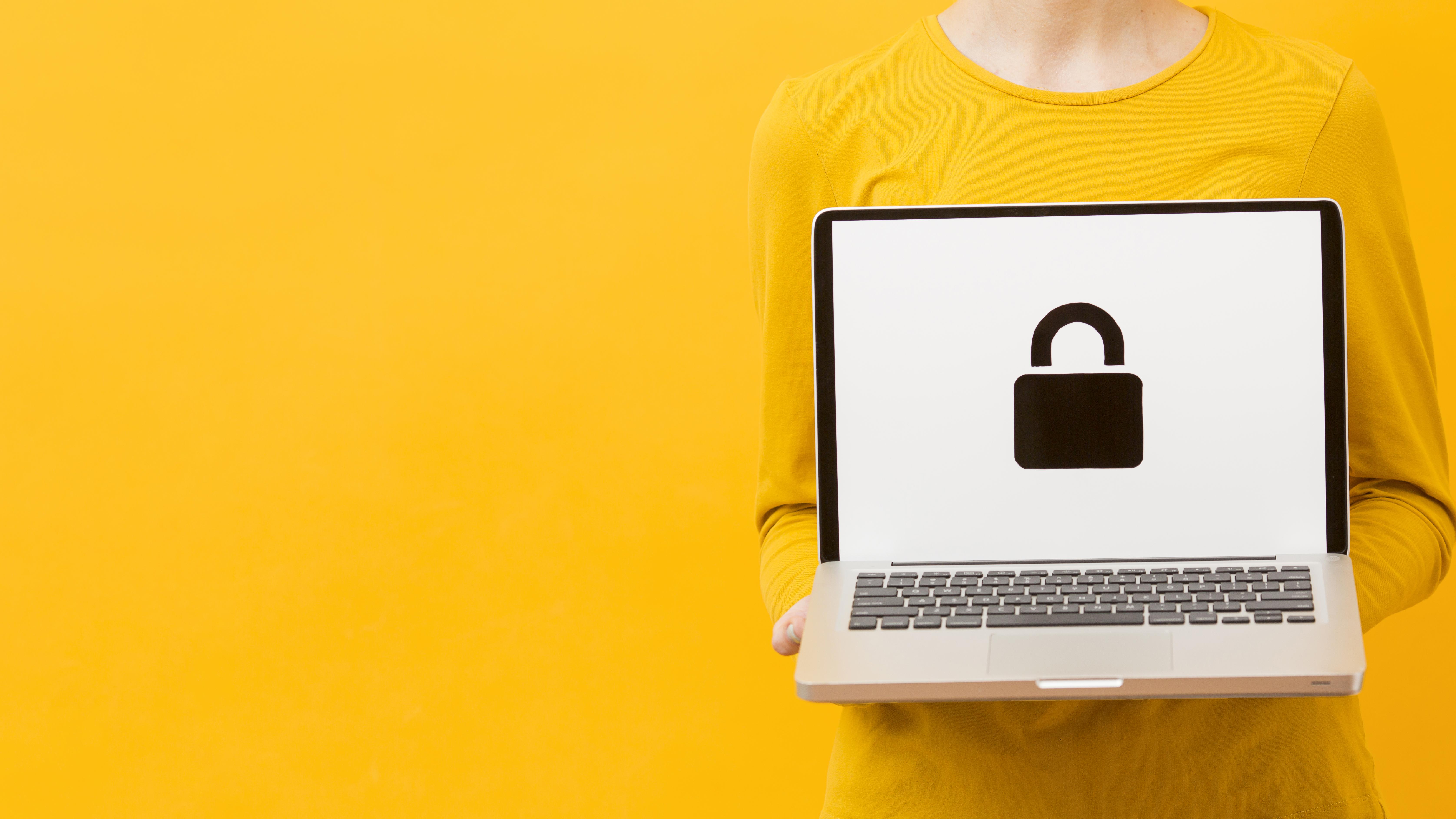 Photograph of a woman wearing yellow clothes against a yellow background. She is holding a laptop. On the screen is a padlock symbol.