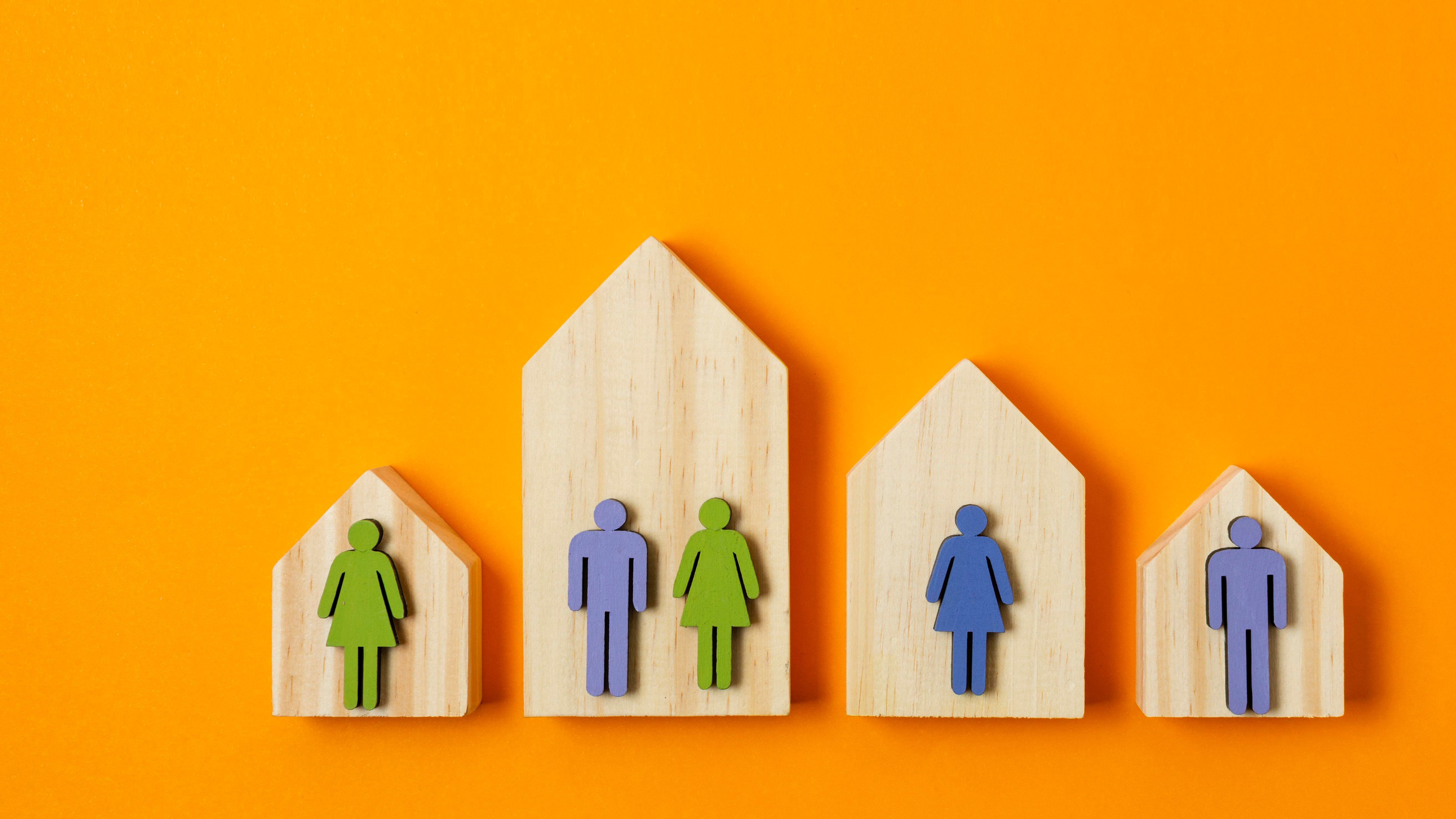 photo of four wooden house shapes on an orange surface. Each house also has one or two wooden cut-out people shapes overlaid