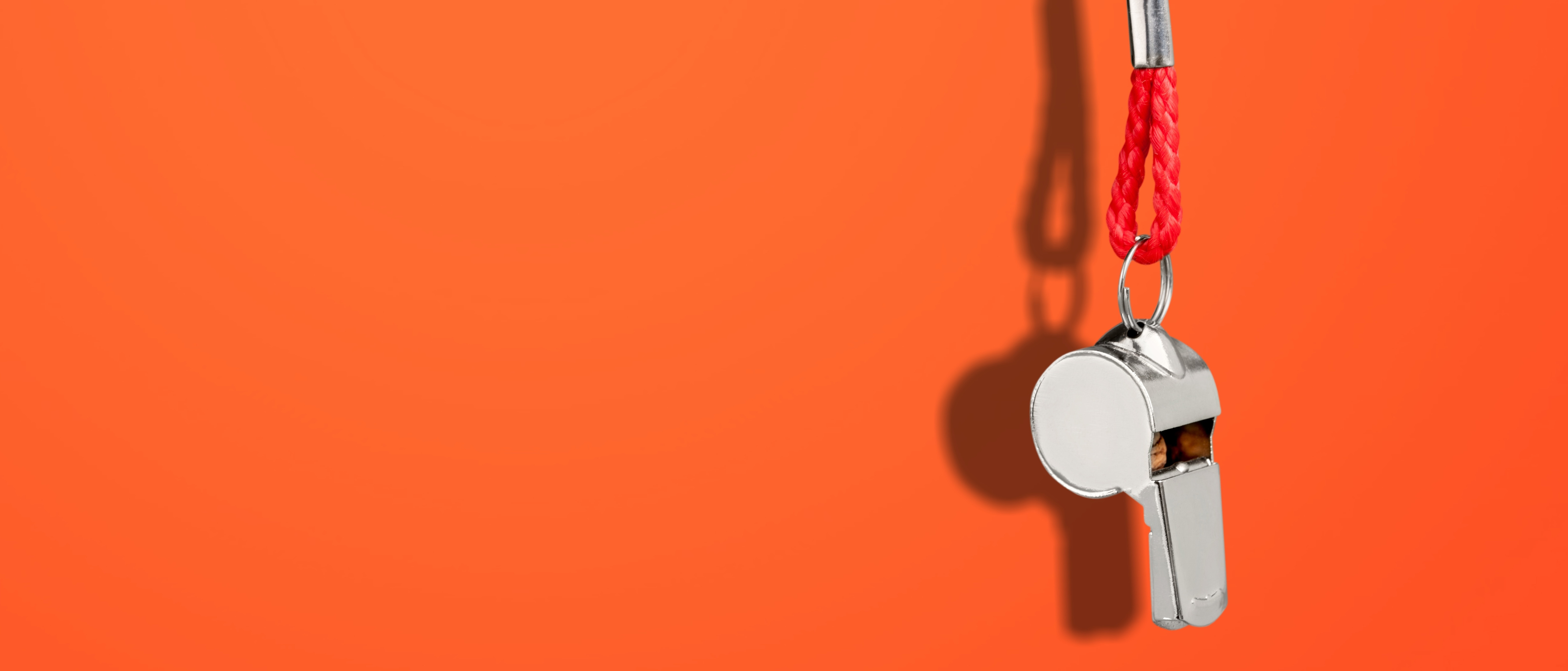 A metal whistle dangling on a red cord in front of a red background