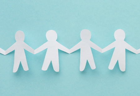 Photo of a paper chain shaped like a row of people cut out of white paper lying on a turquoise surface