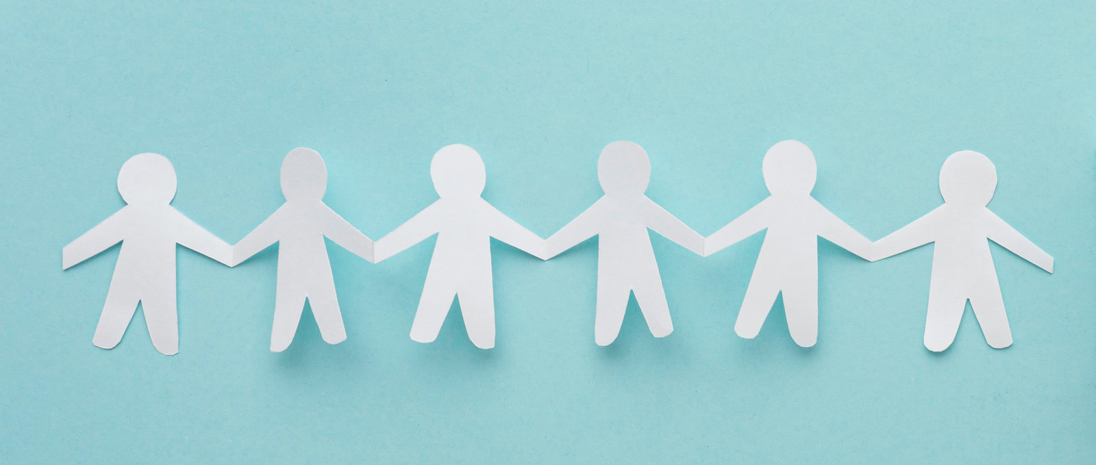 Photo of a paper chain shaped like a row of people cut out of white paper lying on a turquoise surface
