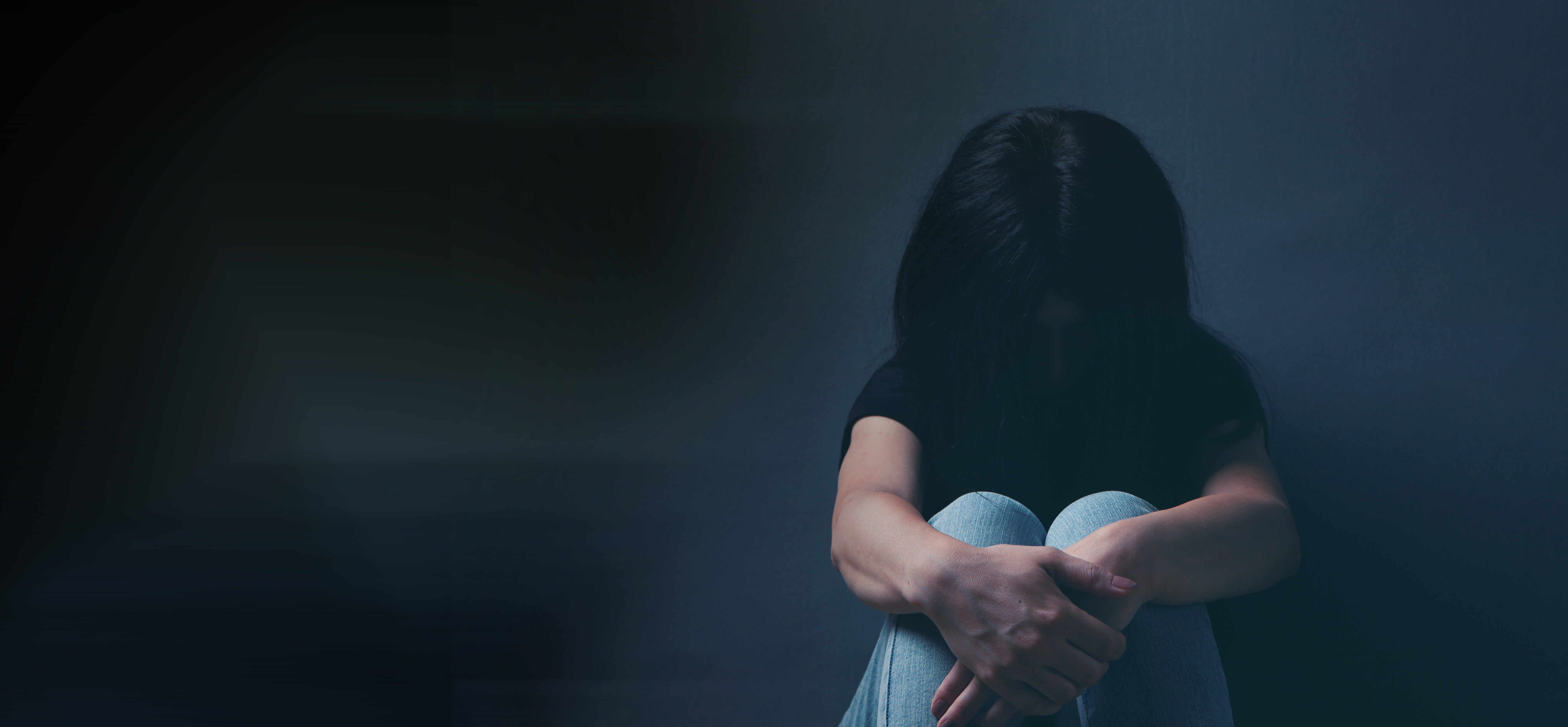 Woman sat on the floor in a dark room with her legs tucked in and her head down