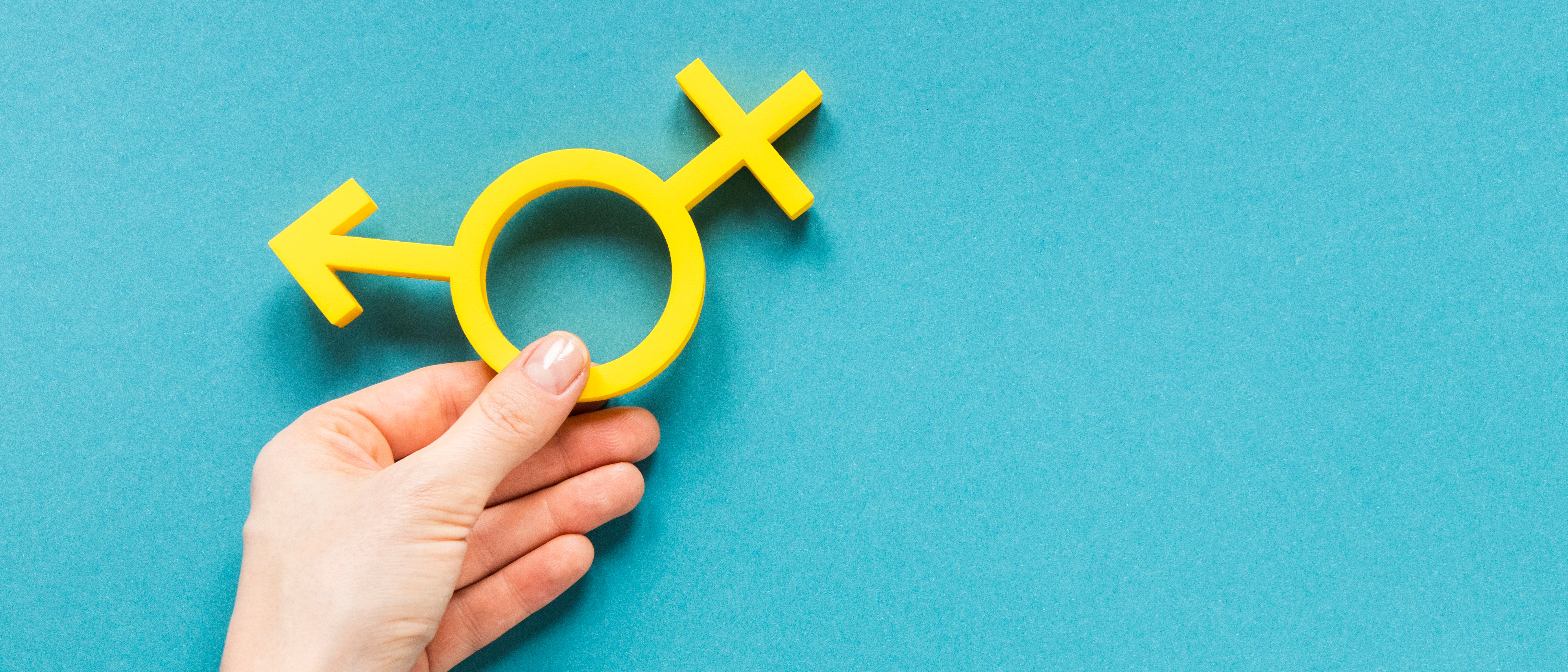 Close-up of a hand holding a yellow hybrid symbol of male and female gender symbols. 