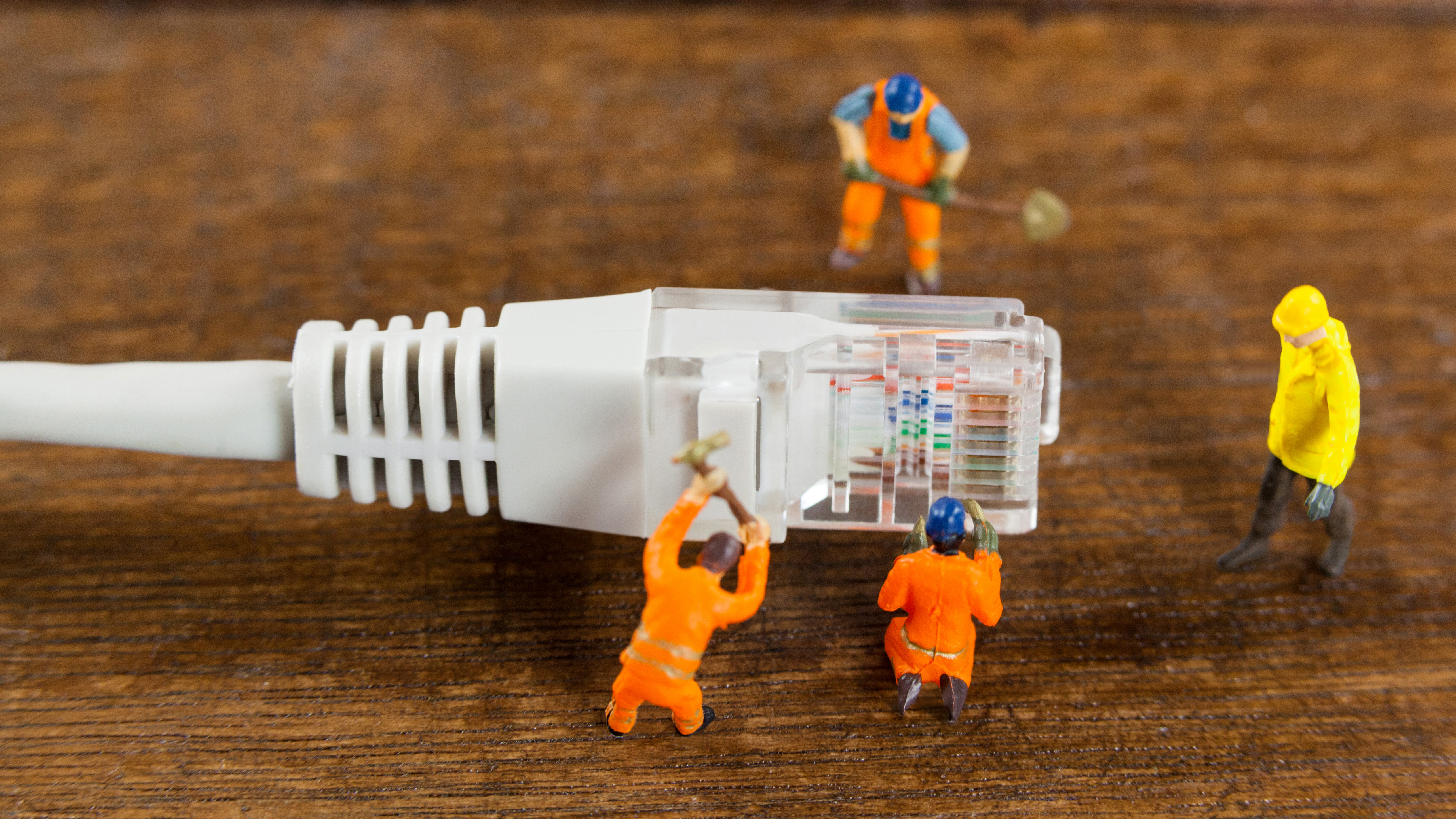 Super close up photo of a computer ethernet plug with four tiny models of 'engineers' working around it