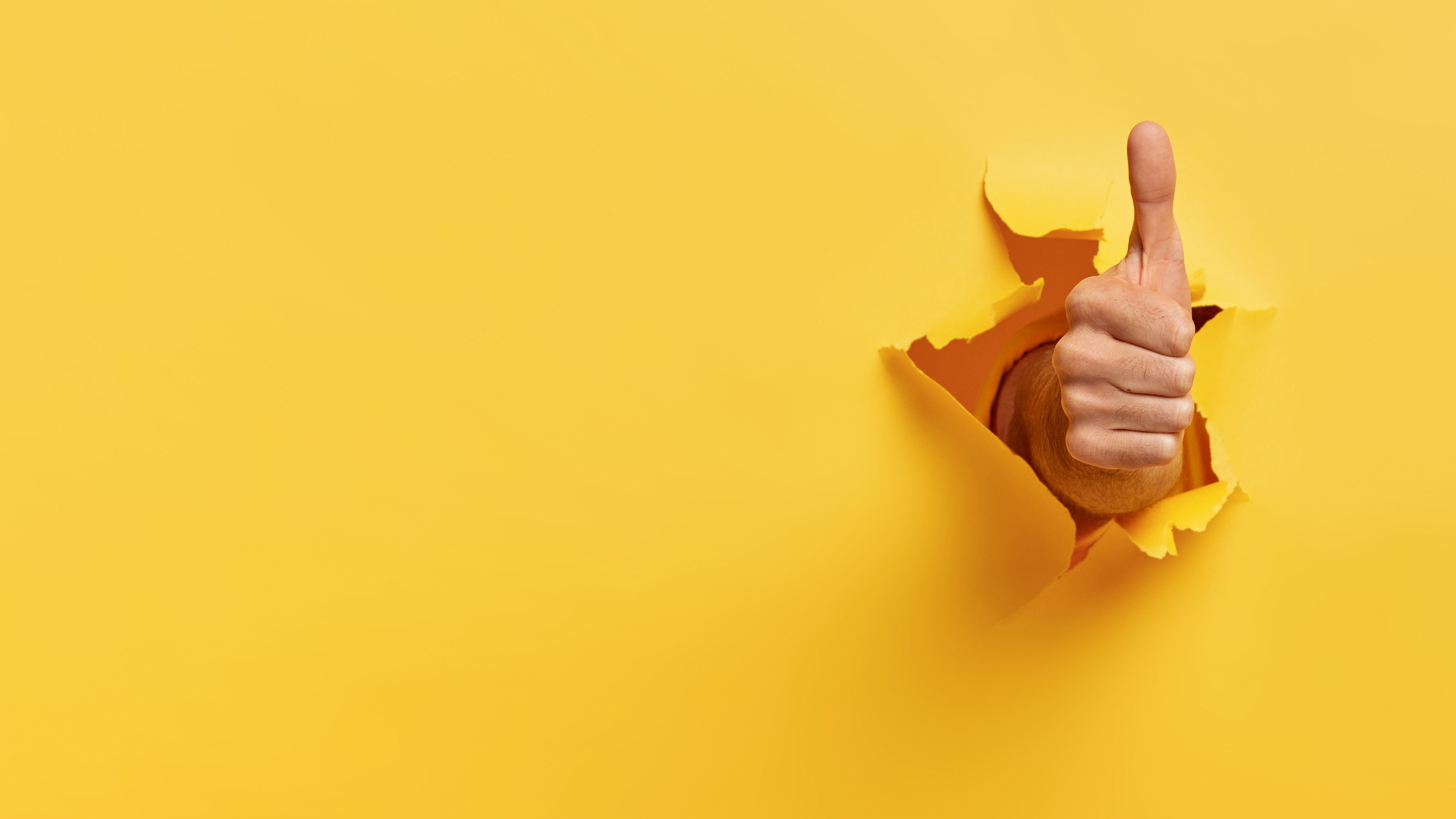 Photo of a hand with the thumb pointing up in a positive gesture that looks like it has been pushed through the yellow background