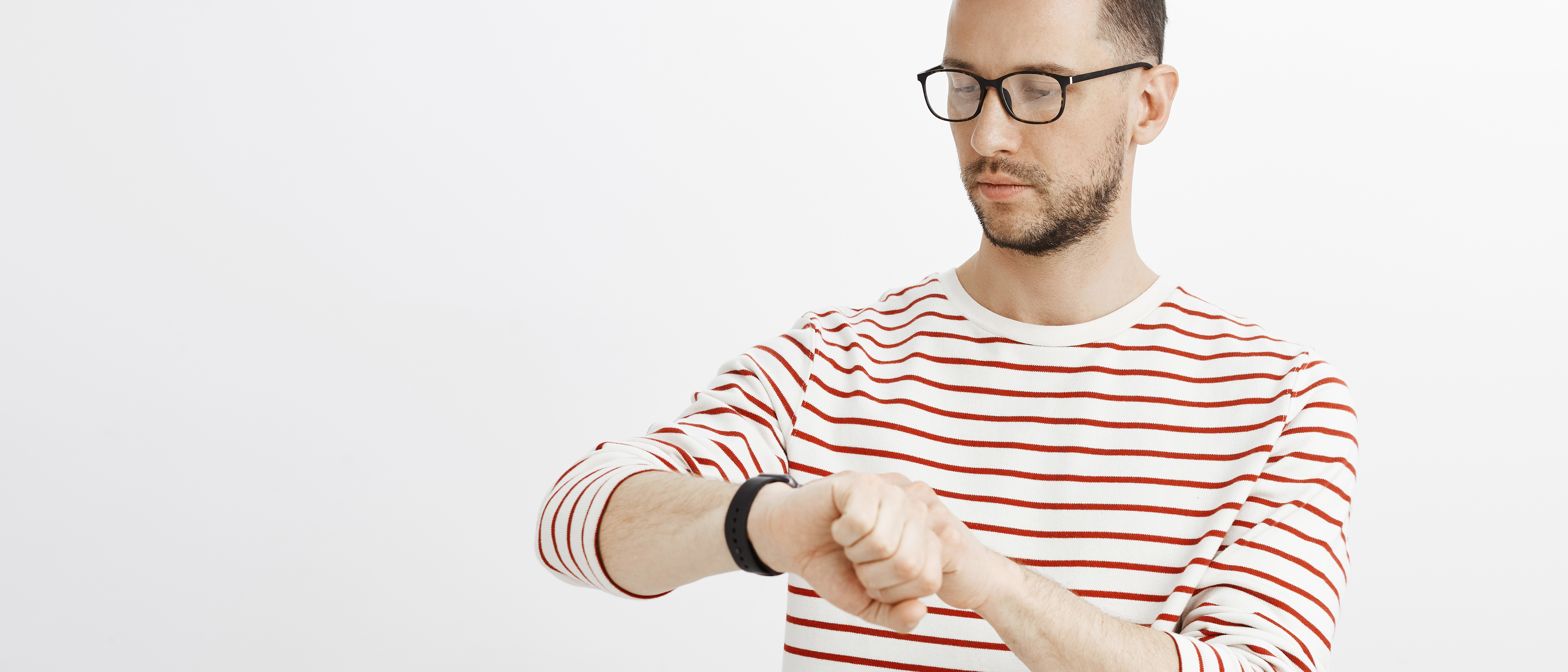 Photo of a young man in a red and white striped top looking impatiently at his watch