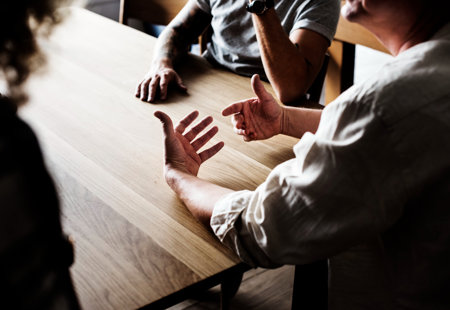 People gathered together, sitting at a table, mainly showing their hands.