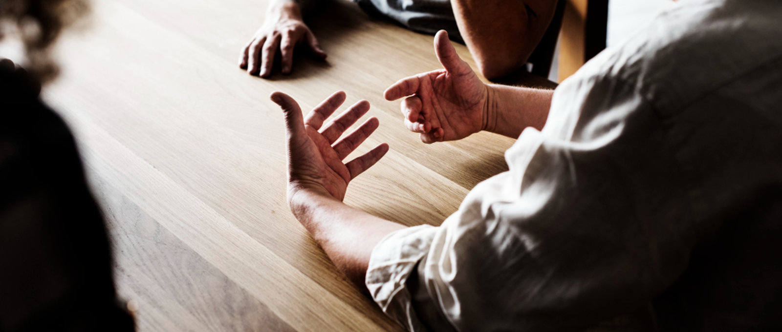 People gathered together, sitting at a table, mainly showing their hands.