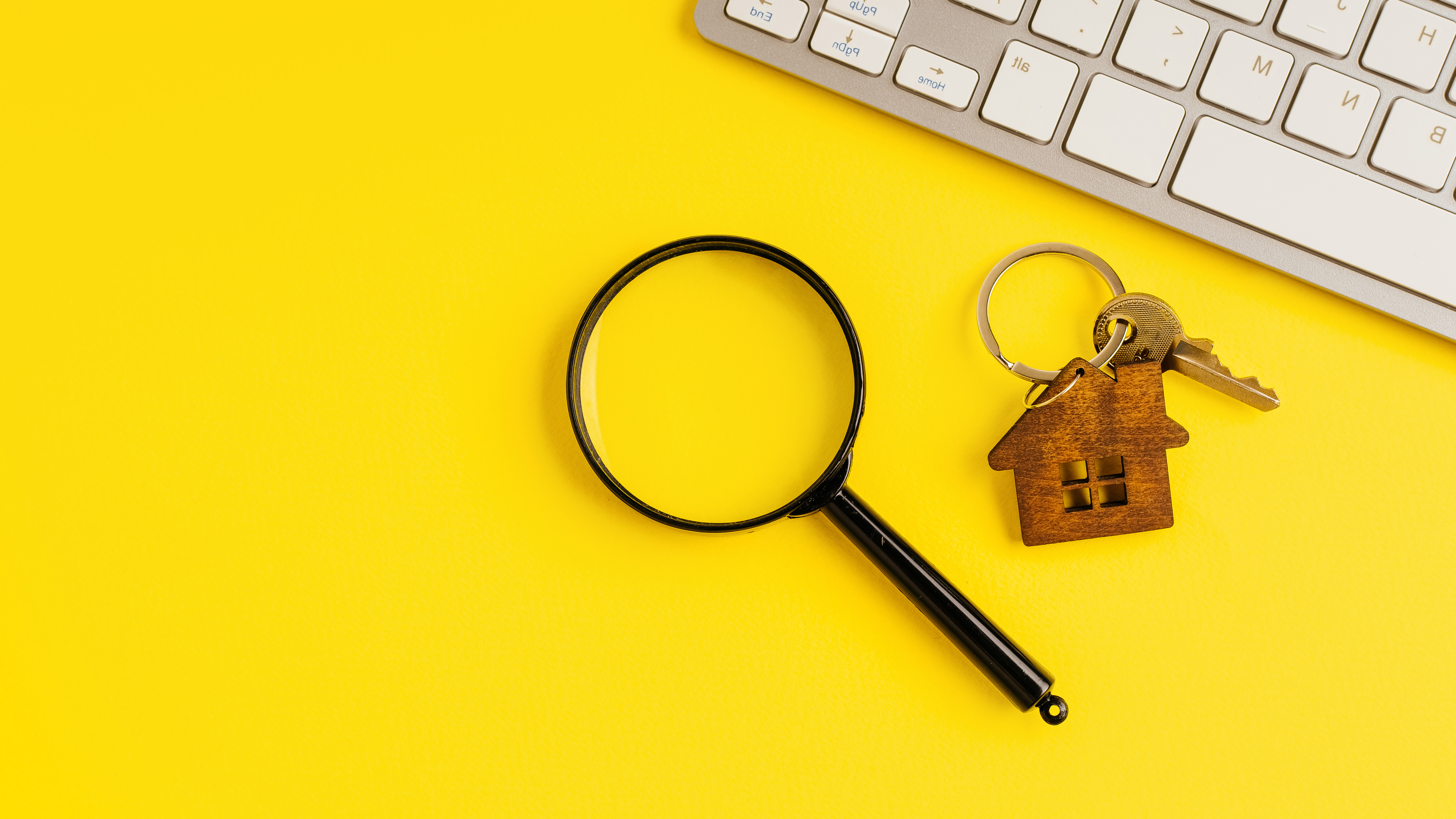 photo of a magnifying glass, a set of house keys, and a keyboard on a bright yellow surface