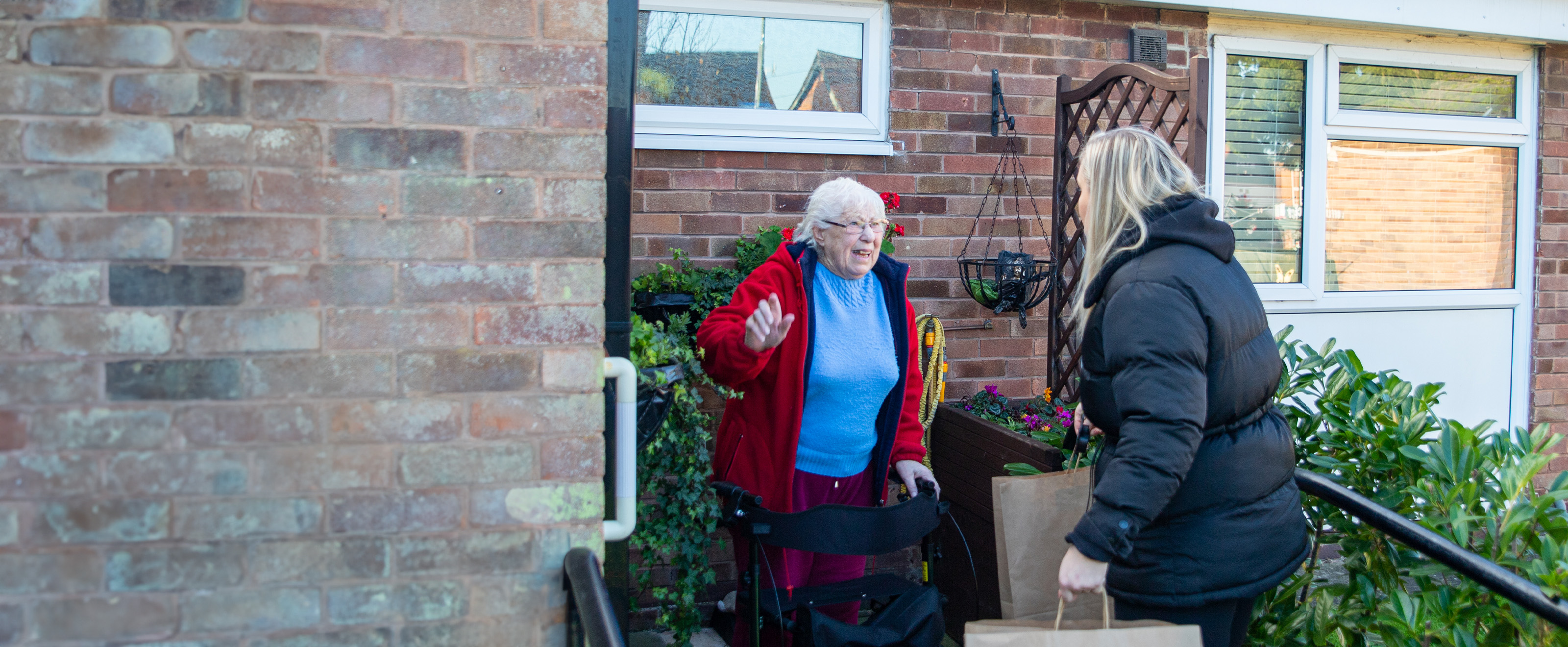 young woman carrying brown paper bag talking with old woman outside a property