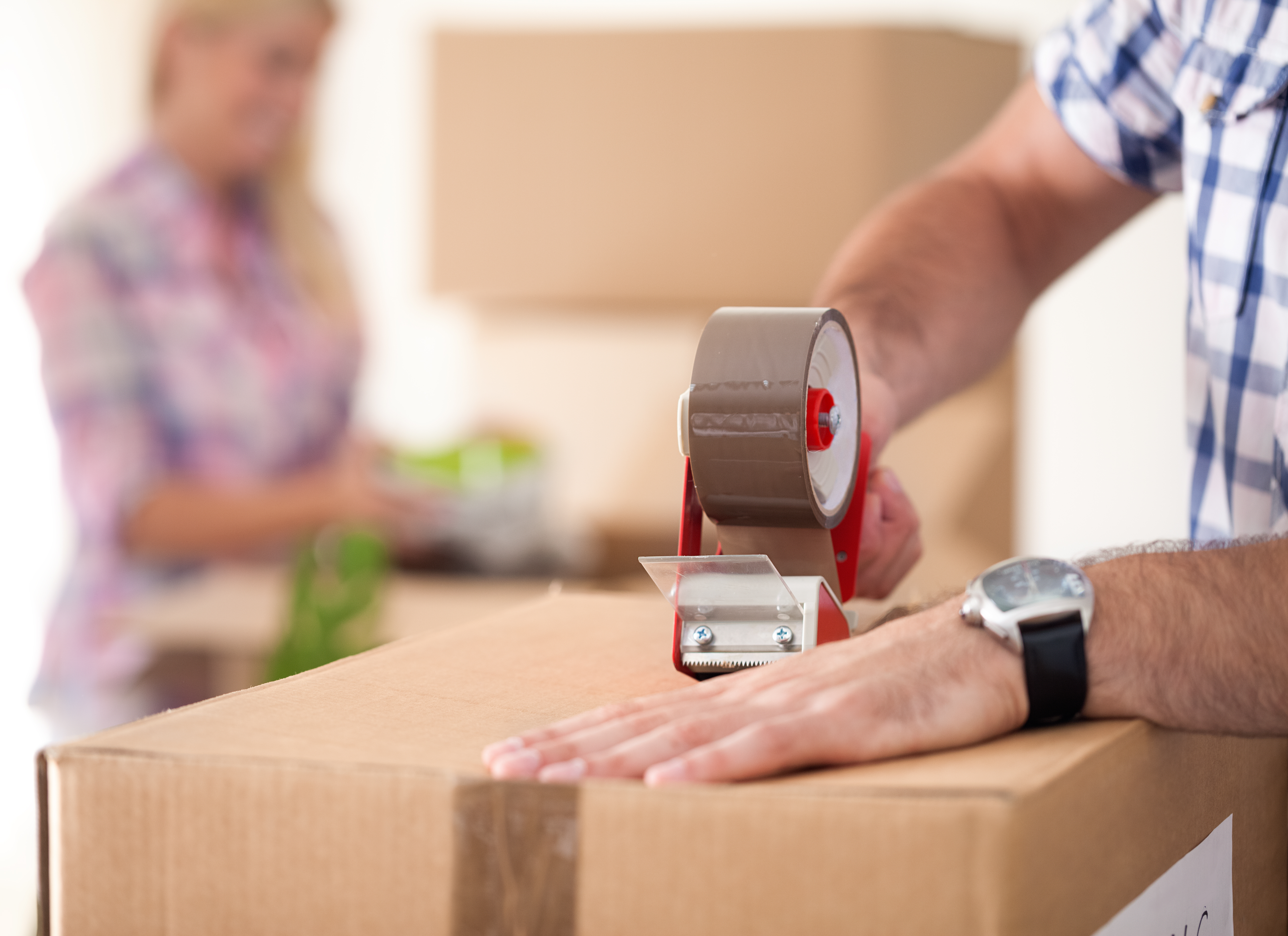 Close up photograph of a man sealing up a packing box with tape.